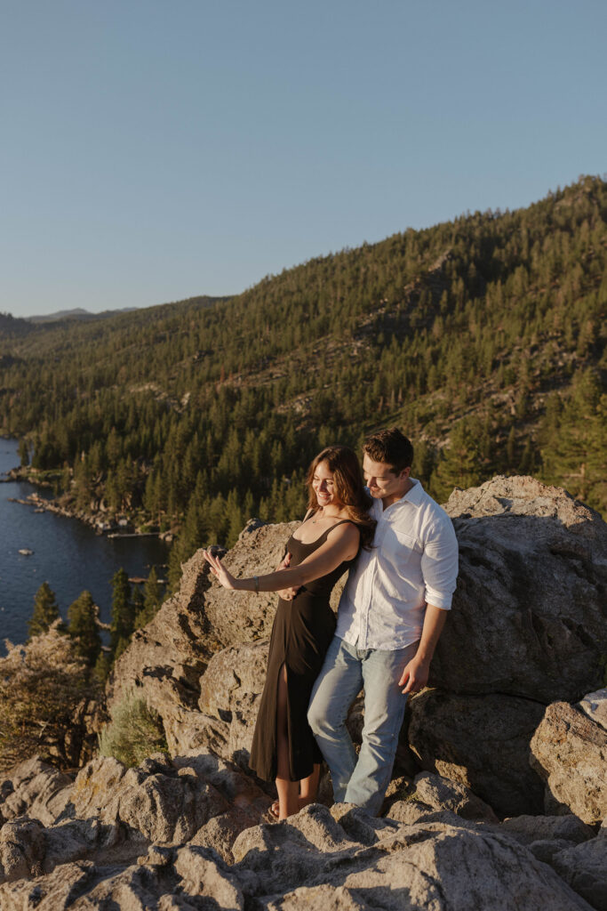 Engagement couple admiring engagement ring on woman's hand while leaning on rock together at Eagle Rock in Lake Tahoe