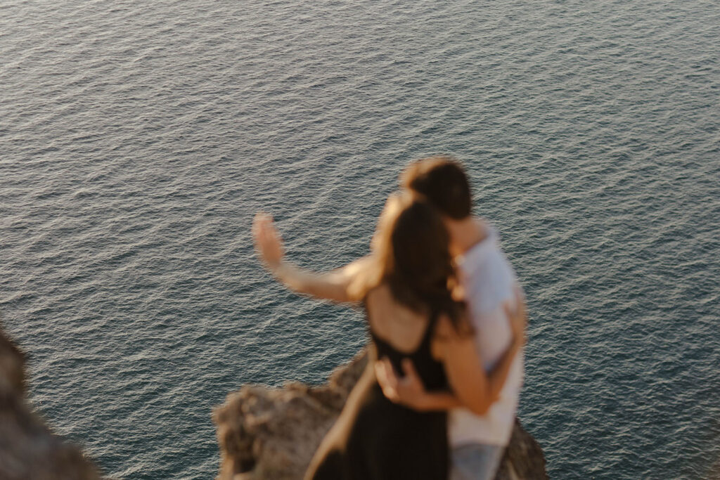 Engagement couple holding each other while admiring engagement ring and looking out over Lake Tahoe at Eagle Rock