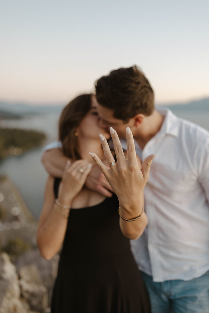 Couple kissing while woman holds up hand to camera with engagement ring at Eagle Rock in Lake Tahoe
