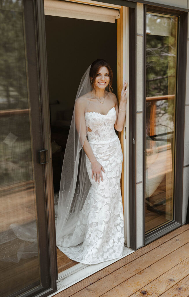 Bride in wedding dress leaning in doorway between windows and smiling at the camera at Nakoma Resort