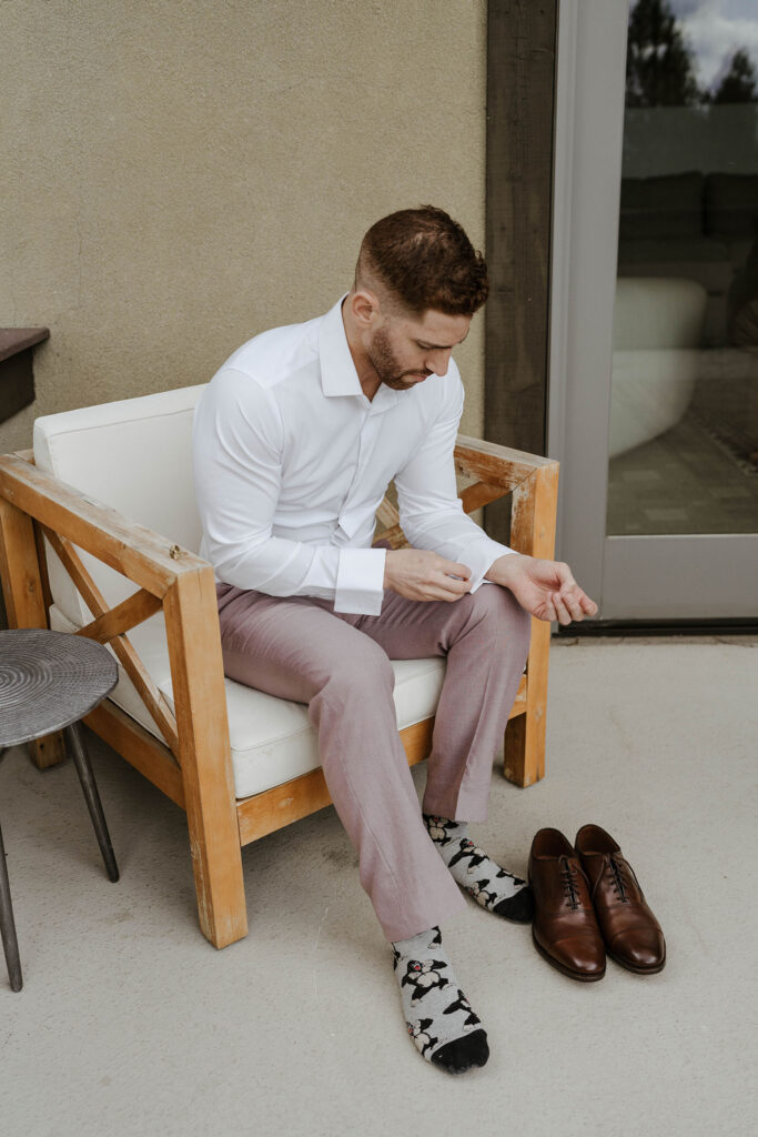Wedding groom sitting in chair and fastening buttons on shirt cuff at Nakoma Resort