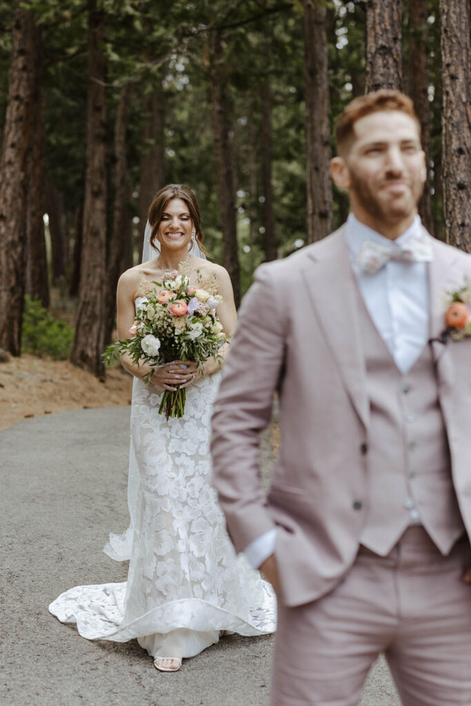 Wedding bride holding colorful floral bouquet while smiling and walking up behind groom during first look at Nakoma Resort