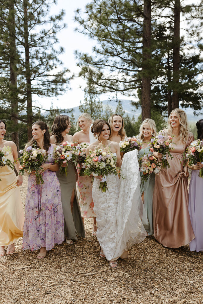 Wedding bride and bridesmaids walking together towards camera while holding colorful floral bouquets and smiling at Nakoma Resort
