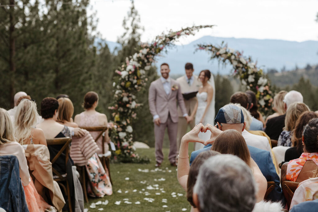 Wedding guest holding up a heart with her hands towards couple during ceremony at Nakoma Resort