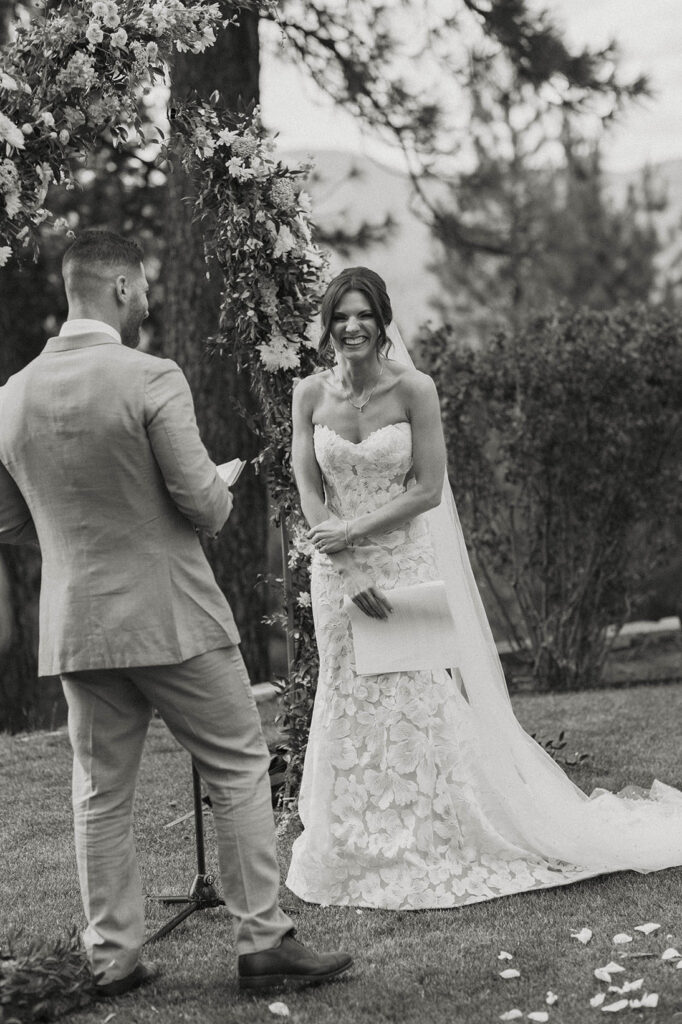 Bride laughing and looking over at camera while groom reads vows during ceremony at Nakoma Resort