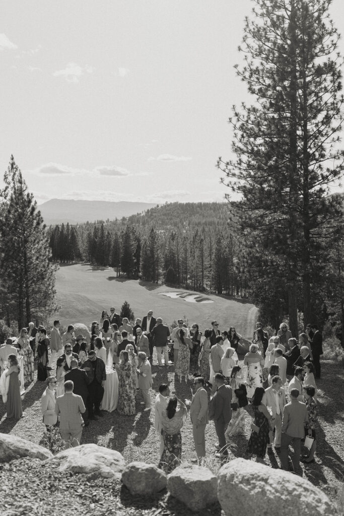 Wedding guests enjoying cocktail hour with grass field and forest of pine trees behind them at Nakoma Resort