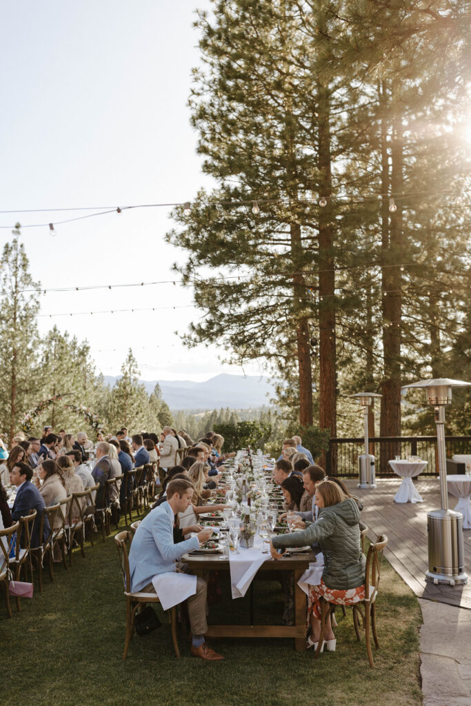 Wedding guests sitting at long wooden dinner table and eating at Nakoma Resort
