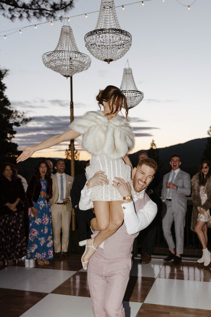 groom holding his bride on his shoulders at sunset