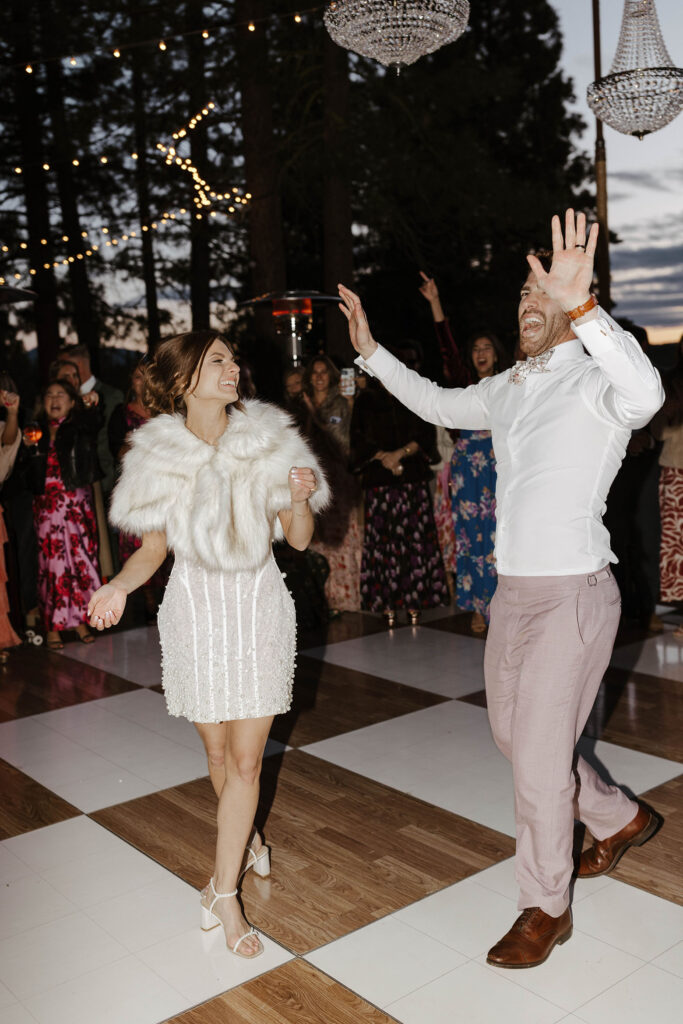Wedding couple dancing together on checkered dance floor with guests celebrating behind them and string lights in background at Nakoma Resort
