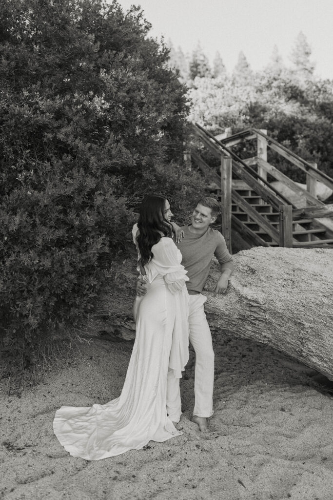 engagement couple leaning on a rock in lake tahoe smiling