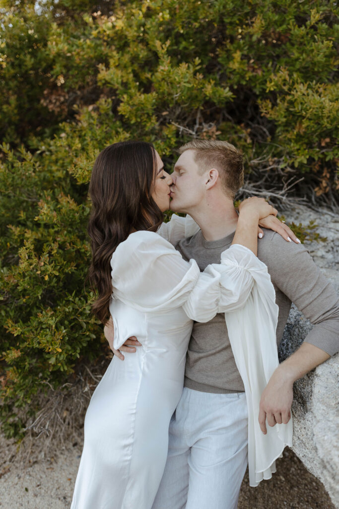 man leaning on a rock in lake tahoe kissing a woman