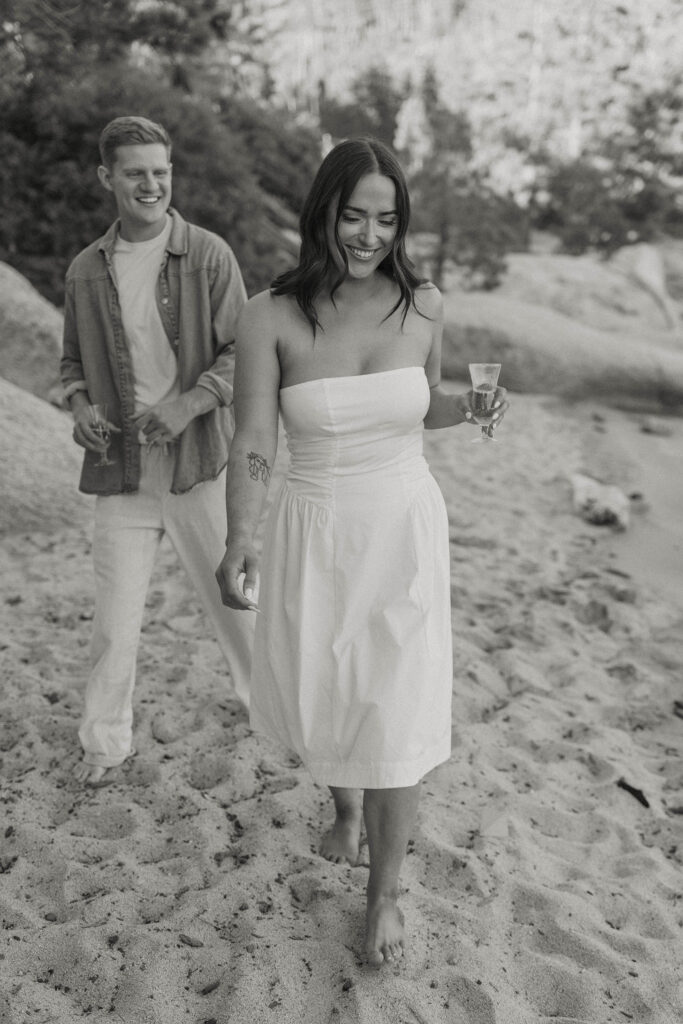 couple walking towards the camera laughing holding champagne in lake tahoe