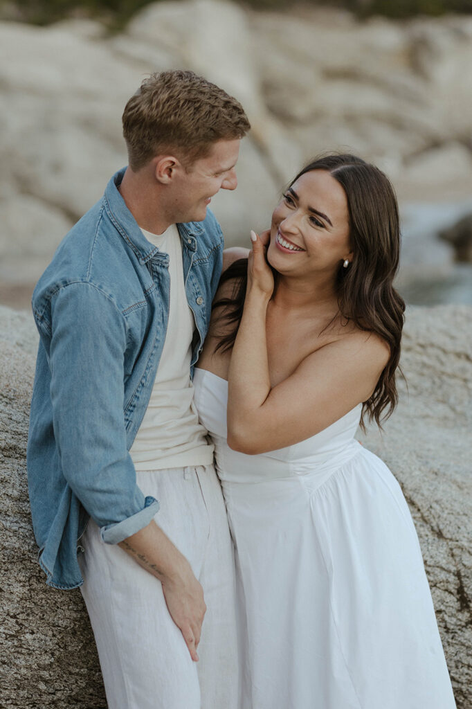 couple laughing as they lean on a rock in lake tahoe
