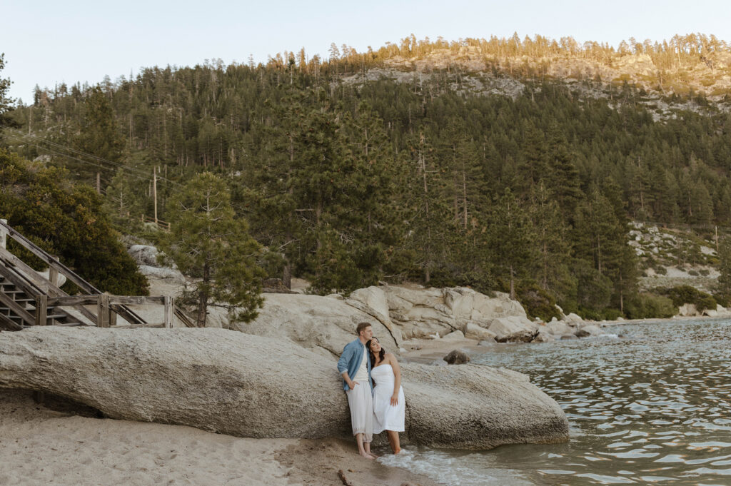 couple leaning on a rock looking at the water in lake tahoe with the mountains in the distance