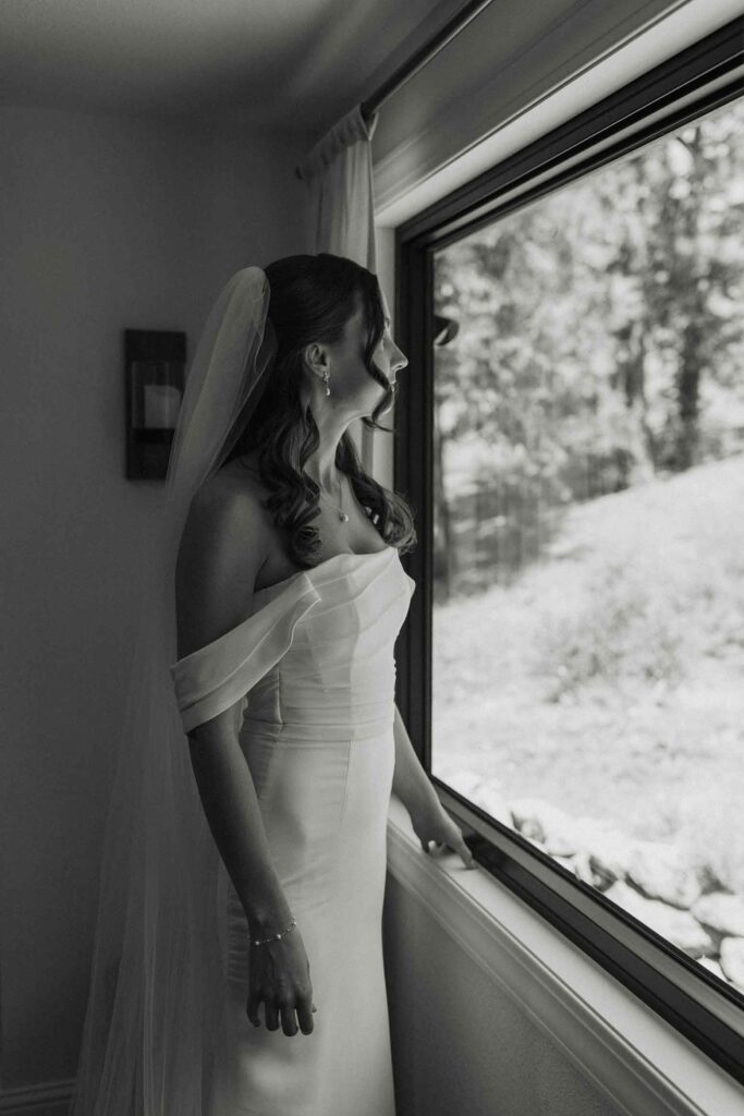 Elopement bride in wedding dress looking out window while resting hand on ledge in South Lake Tahoe