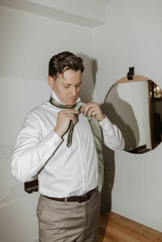 Elopement groom tying tie while inside at South Lake Tahoe