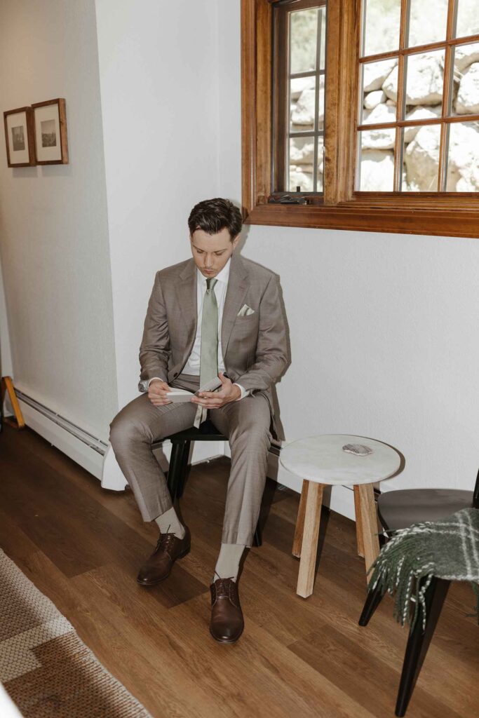 Elopement groom sitting on chair and reading vow book while inside at South Lake Tahoe