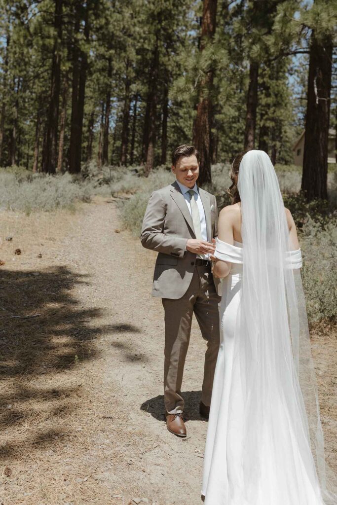 Elopement groom smiling while turning around to see wedding bride during first look at South Lake Tahoe with pine trees in background