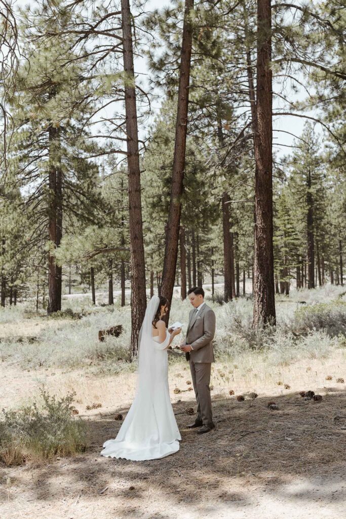 Groom holding bride's hands while she reads wedding vows during first look in South Lake Tahoe with pine trees in background