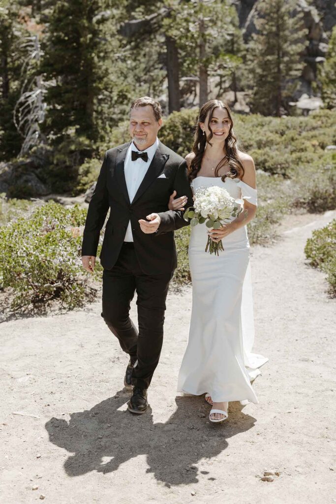 Bride walking down aisle to elopement ceremony while holding dad's arm in South Lake Tahoe