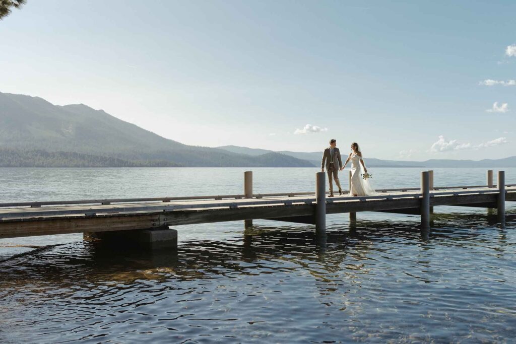 Elopement couple holding hands while walking along pier in South Lake Tahoe together while surrounded by water