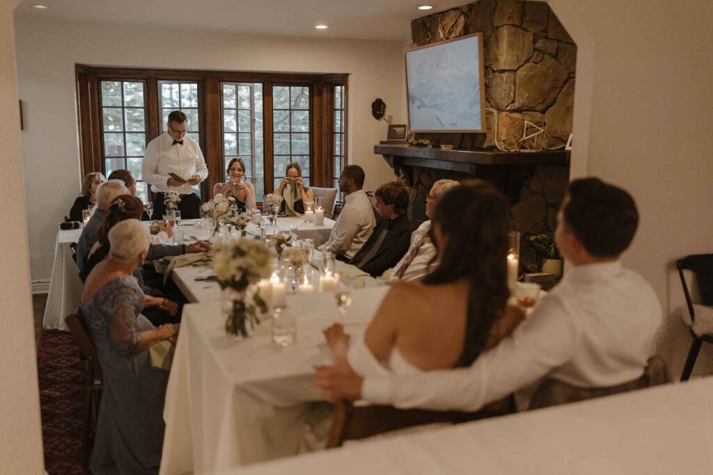 Elopement couple sitting at reception table with groom's arm around bride while listening to speeches at South Lake Tahoe