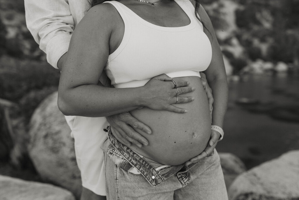 Close up of married couple's hands holding pregnant wife's belly in Lake Tahoe