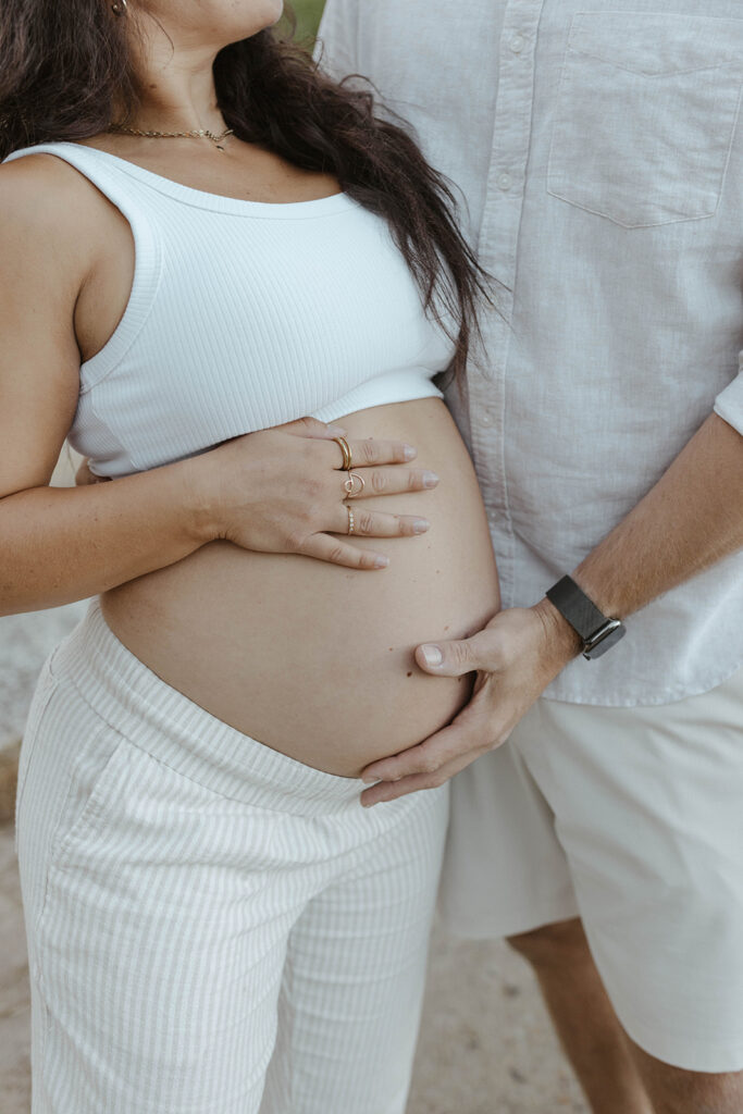 Close up of married couple's hands holding wife's pregnant belly in Lake Tahoe