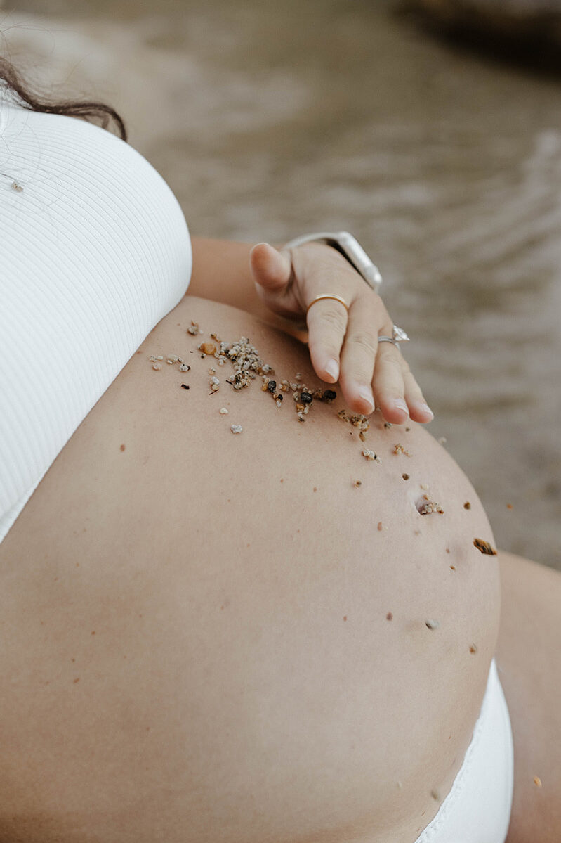 Close up of pregnant woman spreading sand across her belly on Lake Tahoe beach