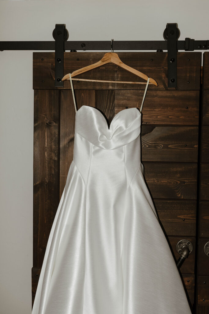 Wedding dress hanging from wooden hanger in front of dark wooden door at The Landing Tahoe Resort in Lake Tahoe