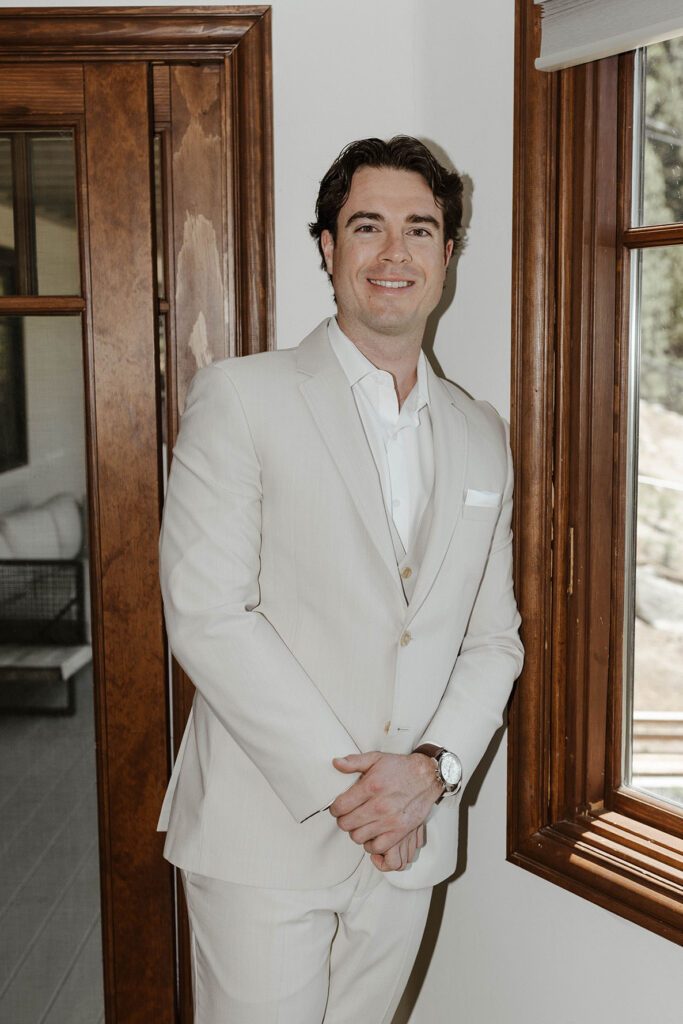 Wedding groom leaning next to window while smiling at the camera inside at the Landing Tahoe Resort
