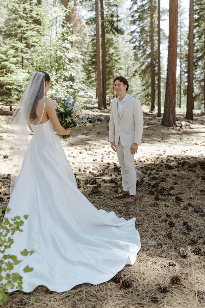 Wedding groom smiling at bride holding flower bouquet with pine trees in background at the Landing Tahoe Resort