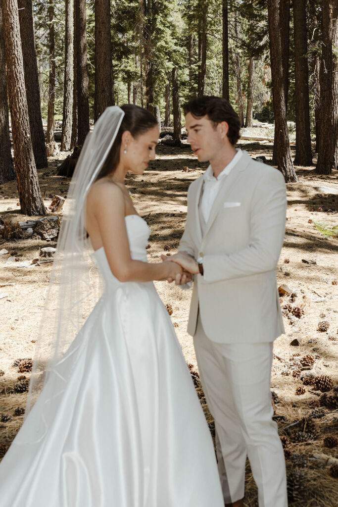 Wedding couple holding hands and talking to each other during first look at the Landing Tahoe Resort with lots of pine trees in background