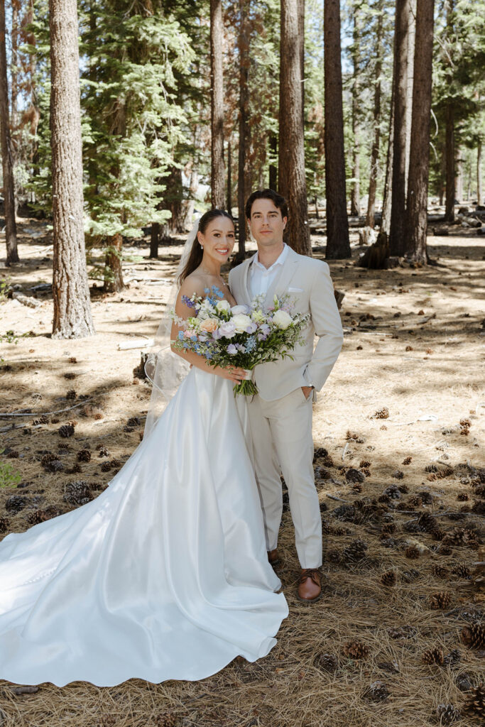 Wedding couple standing together and looking at camera while bride holds floral bouquet with pine trees in background at the Landing Tahoe Resort