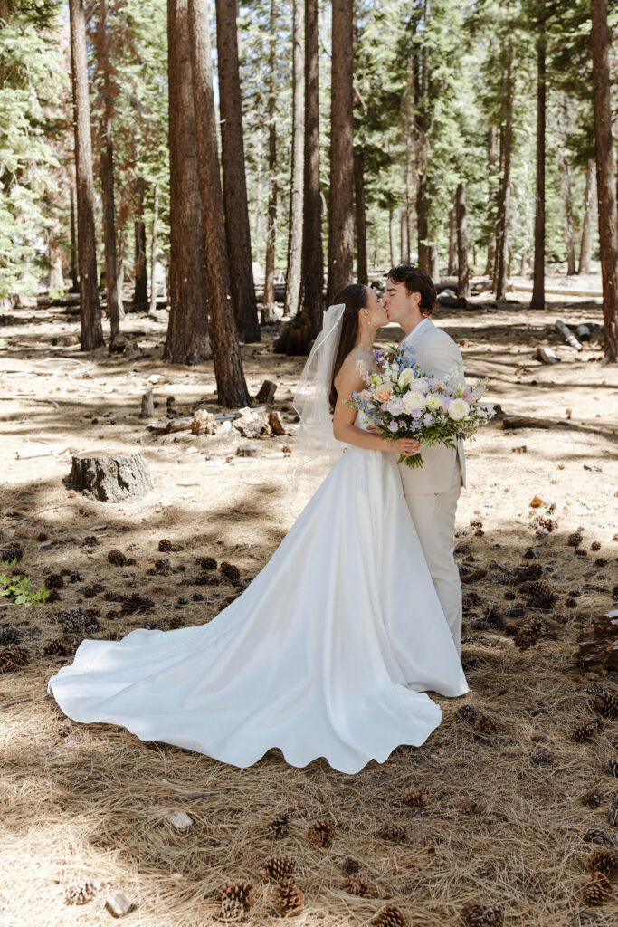 Wedding couple kissing while surrounded by pinecones and pine needles with pine trees in background at the Landing Tahoe Resort
