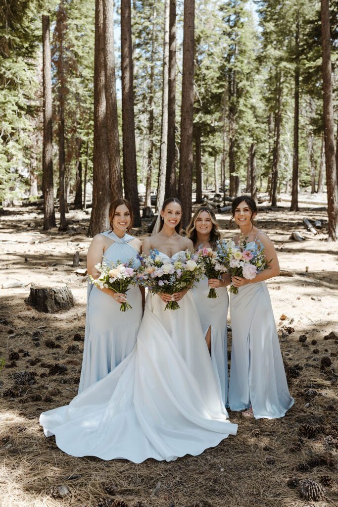 Wedding bride and bridesmaids standing together holding floral bouquets and smiling at the camera with pine trees in background at the Landing Tahoe Resort