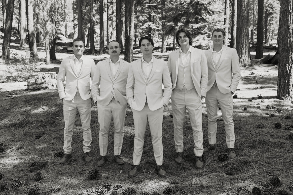 Wedding groom and groomsmen with hands in pockets standing next to each other and facing camera with pine trees in background at the Landing Tahoe Resort