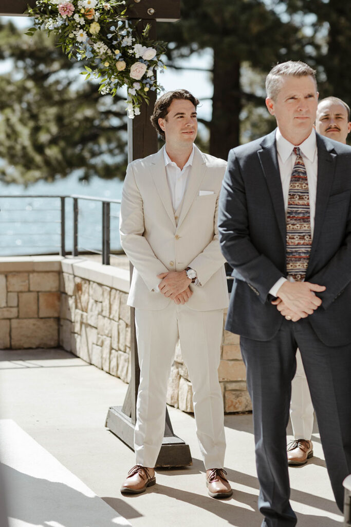 Groom standing in front of wedding arch with hands clasped watching bride walk out at the Landing Tahoe Resort