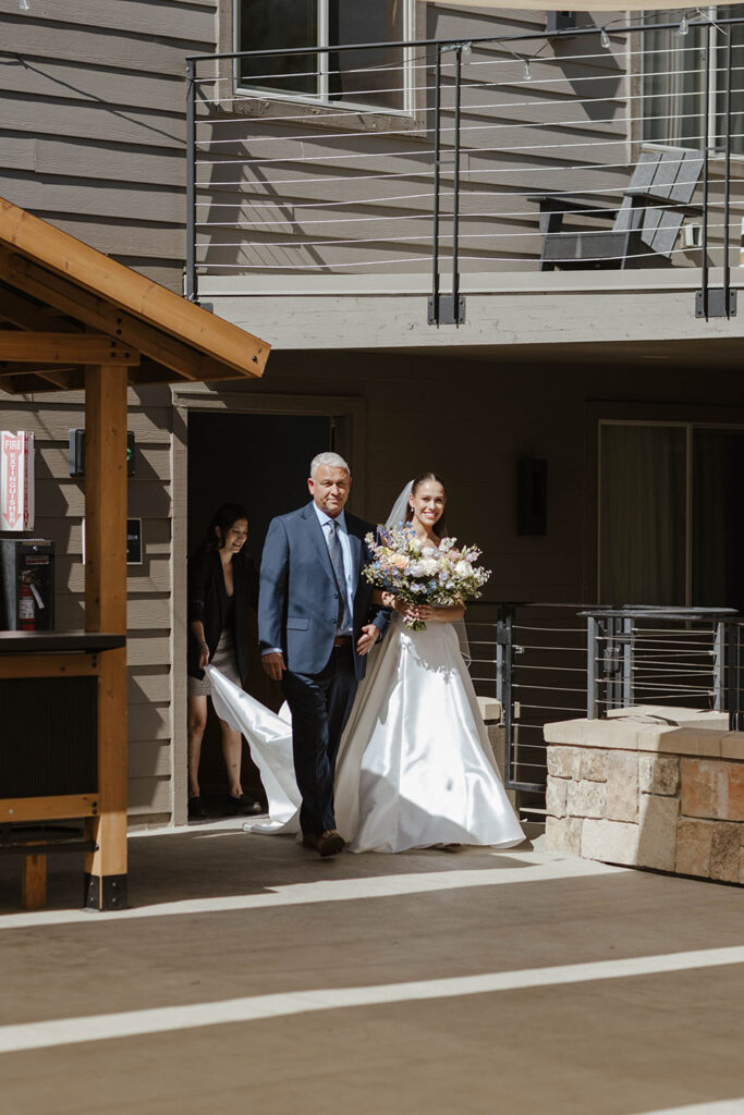 Bride walking to wedding ceremony while holding dad's arm and floral bouquet at the Landing Tahoe Resort