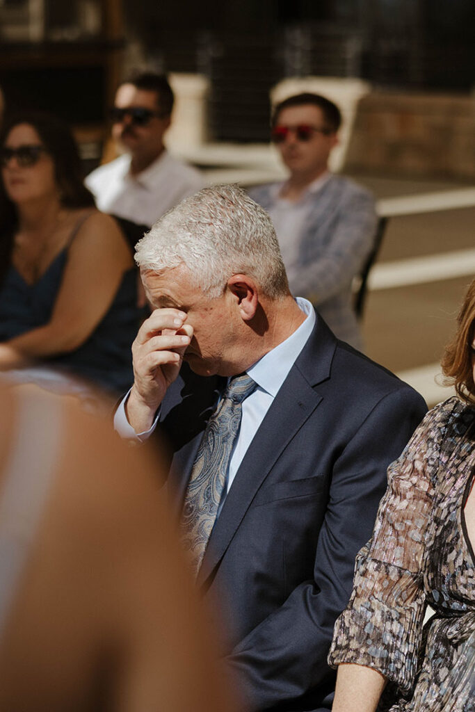 Dad emotional and wiping eyes during wedding ceremony at the Landing Tahoe Resort with guests in background