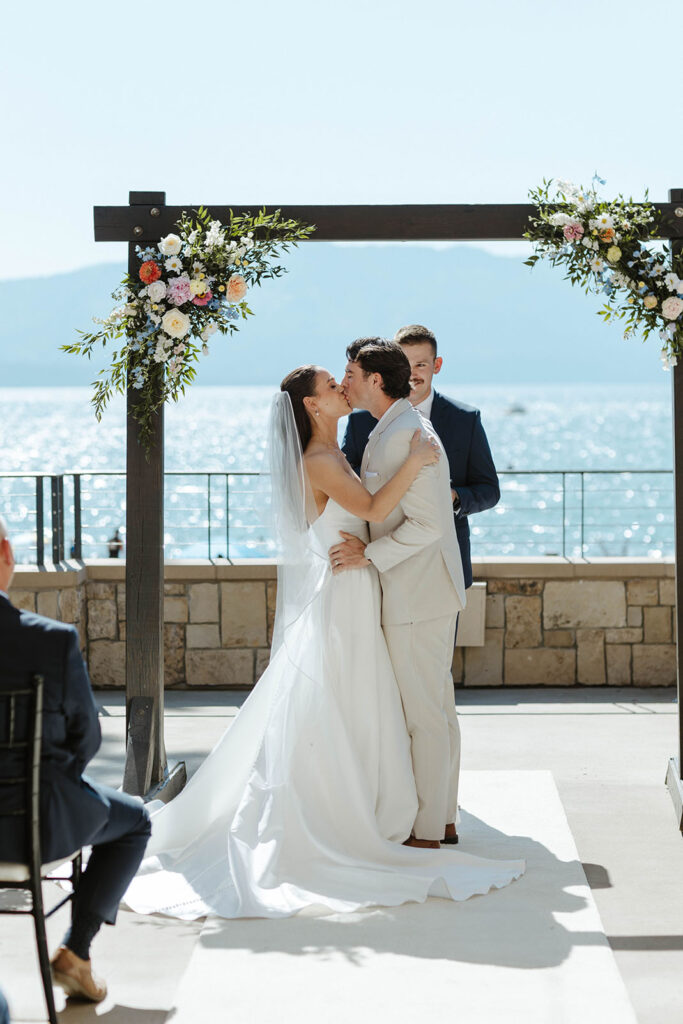 Wedding couple kissing in front of arch after ceremony with Lake Tahoe in background at the Landing Tahoe Resort
