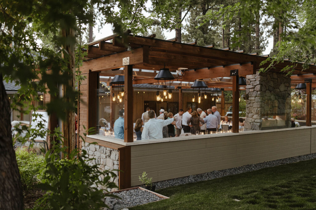 Wedding guests celebrating after ceremony in outdoor wooden patio area with stone fireplace surrounded by greenery at the Landing Tahoe Resort