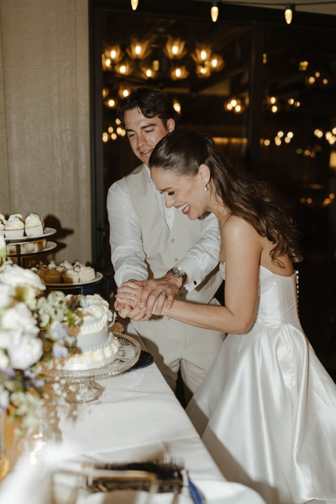 Wedding couple holding knife and cutting cake together with lots of warm lights in background at the Landing Tahoe Resort