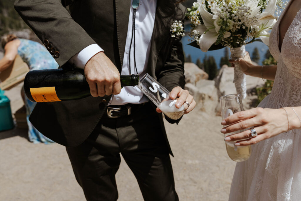Groom pouring champagne into special glasses for elopement couple after ceremony in Lake Tahoe
