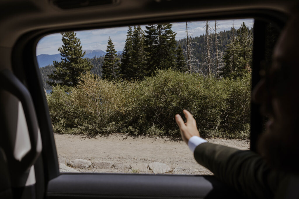 Groom holding hand out of car towards greenery after elopement ceremony in Lake Tahoe