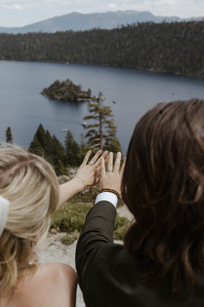 Elopement couple holding hands up together admiring wedding rings in front of Emerald Bay in Lake Tahoe