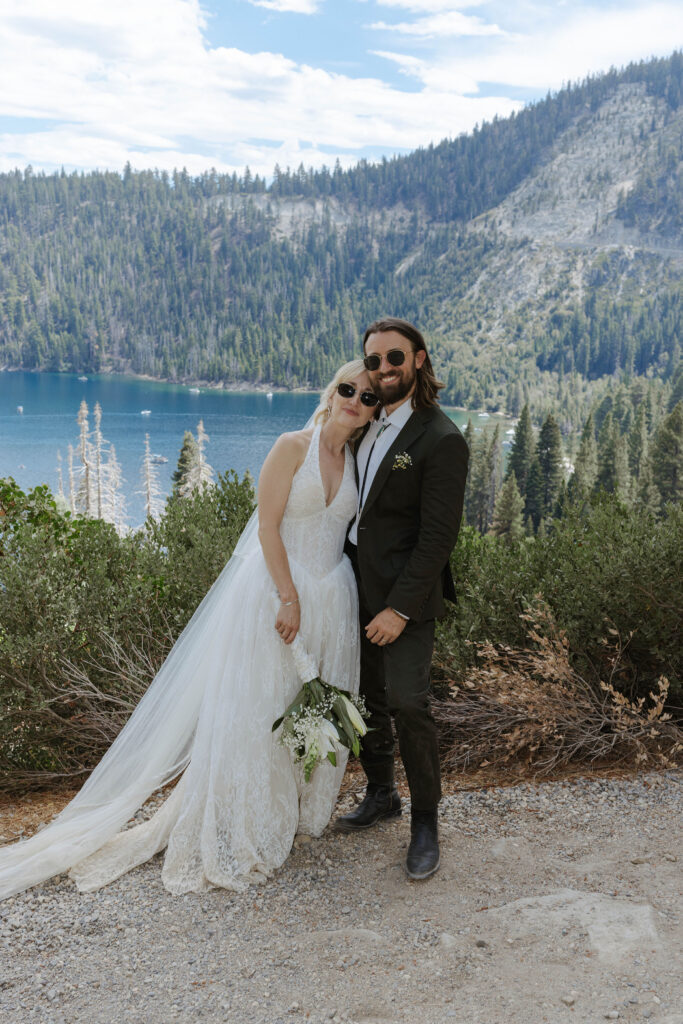 Elopement couple standing together and smiling at camera in front of greenery with Emerald Bay and pine trees in background in Lake Tahoe