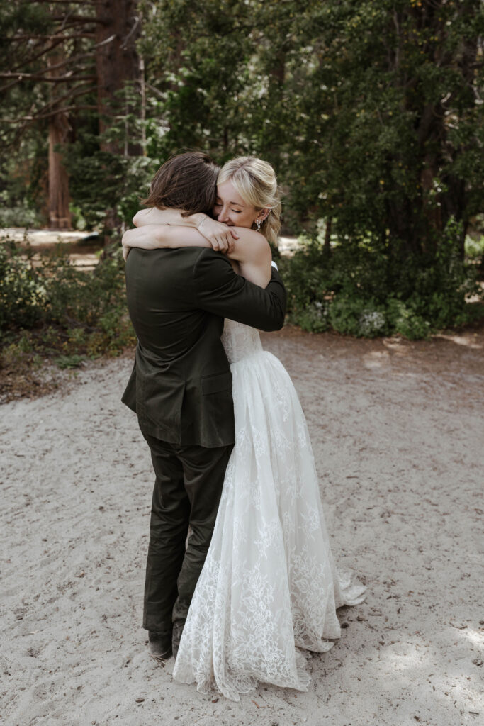 Elopement couple hugging each other while bride has eyes closed on a dirt trail with greenery and pine trees in background in Lake Tahoe