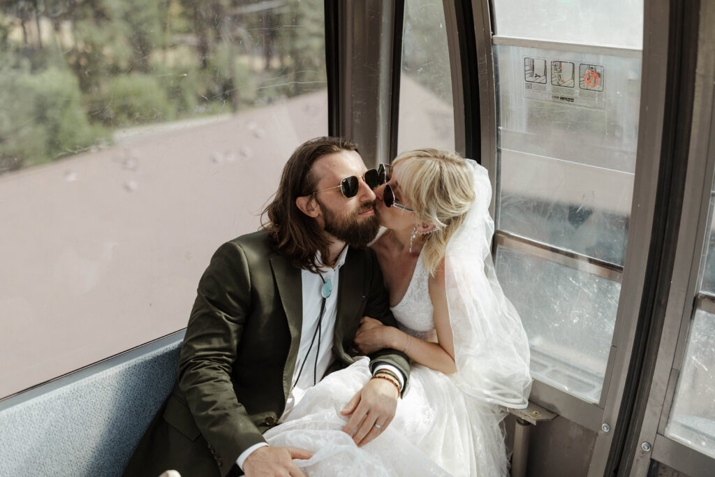 Bride kissing groom's cheek while elopement couple is sitting on bench and riding up Heavenly gondola in Lake Tahoe