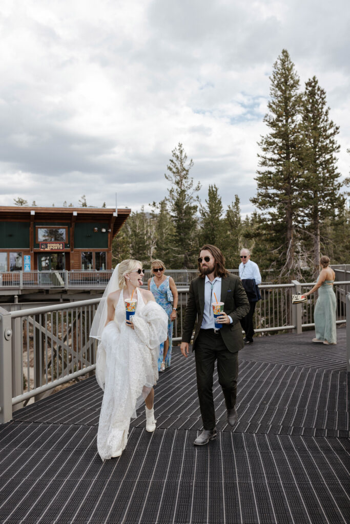 Elopement couple walking together while holding drinks and bride sticks out her tongue at groom with guests walking behind them at Lake Tahoe